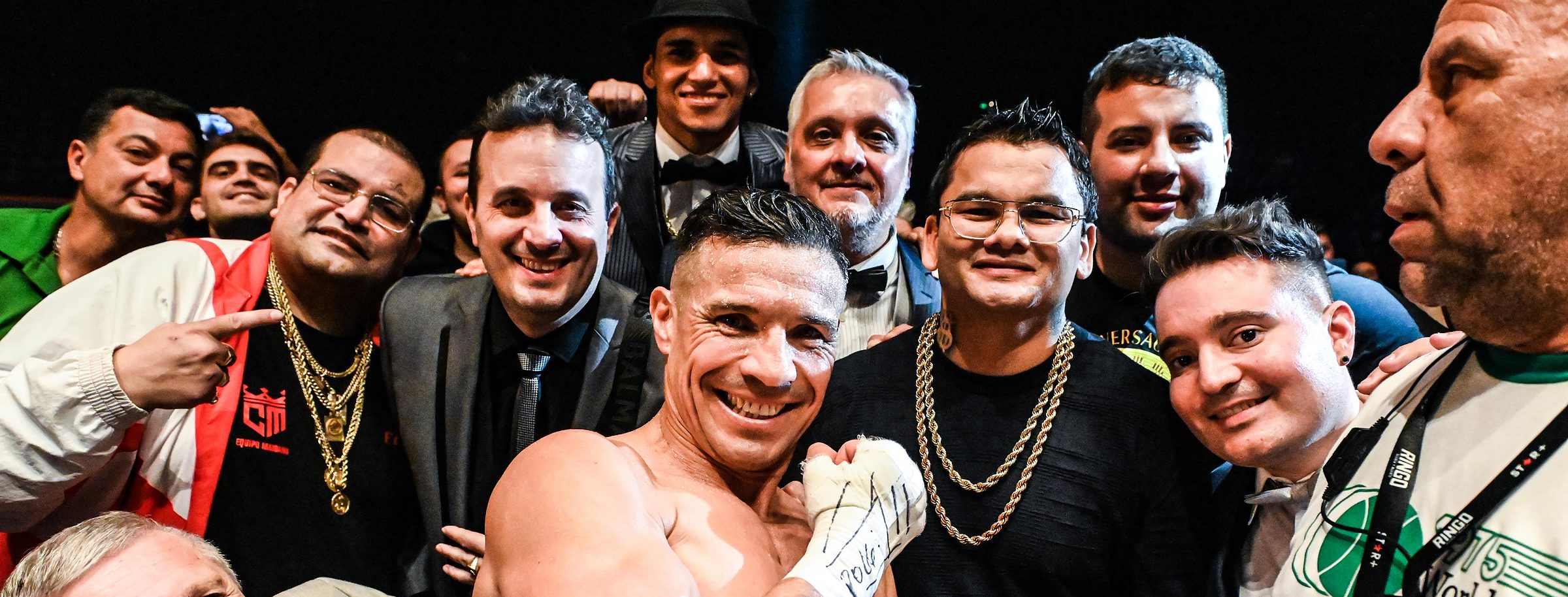 Calabrese, de traje, en el ring entre un grupo que festeja con un boxeador que muestra las vendas firmadas