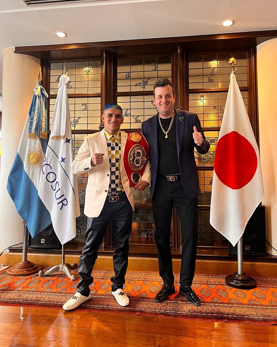 Calabrese, de saco oscuro y con el pulgar arriba, junto a Fernando «Puma» Martínez, que sostiene un cinturón mundial, entre las banderas de Argentina, el Mercosur y Japón