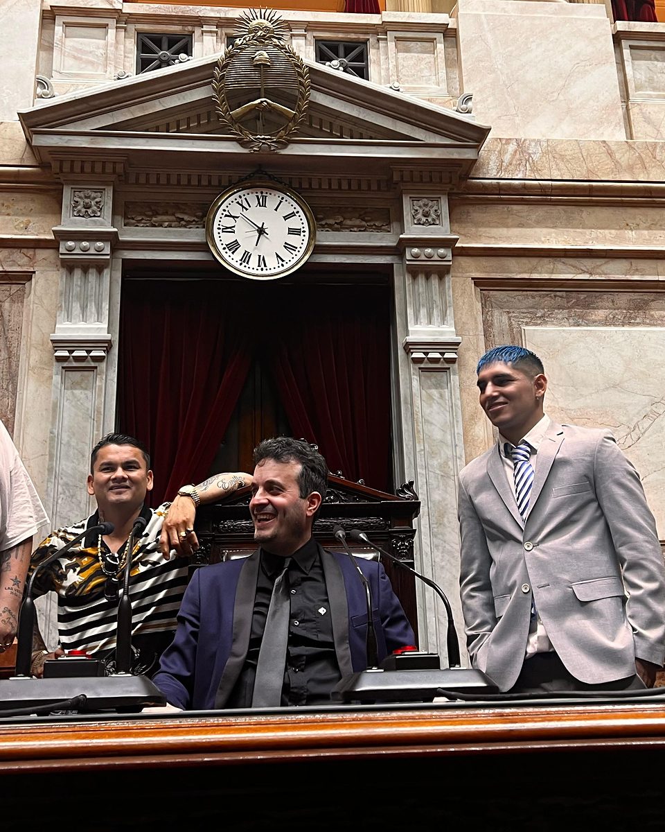 Calabrese sentado en el estrado de la presidencia del recinto de la Cámara de Diputados de la Nación, con dos acompañantes de pie
