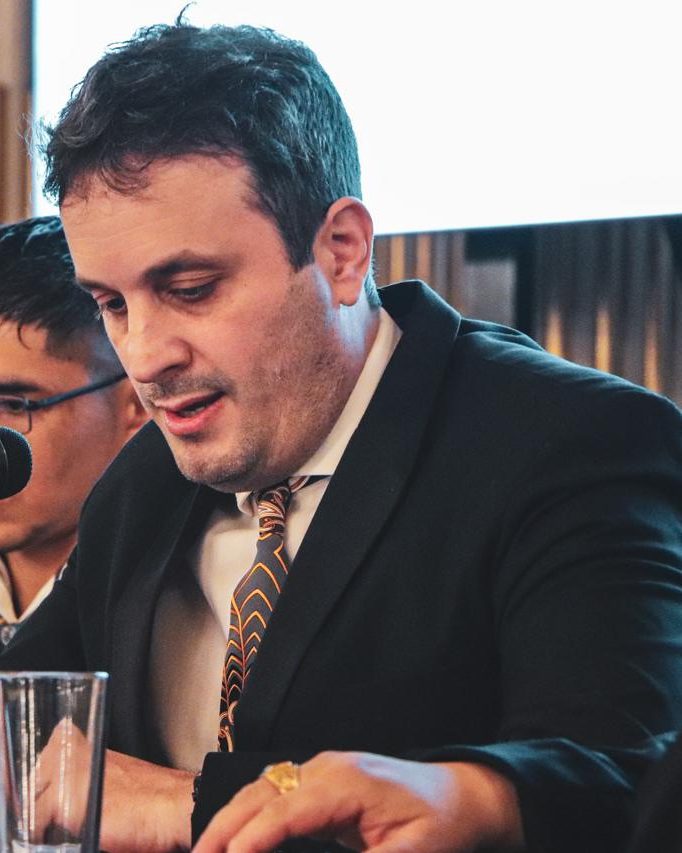 Calabrese, de traje y corbata, habla frente a un micrófono durante un acto