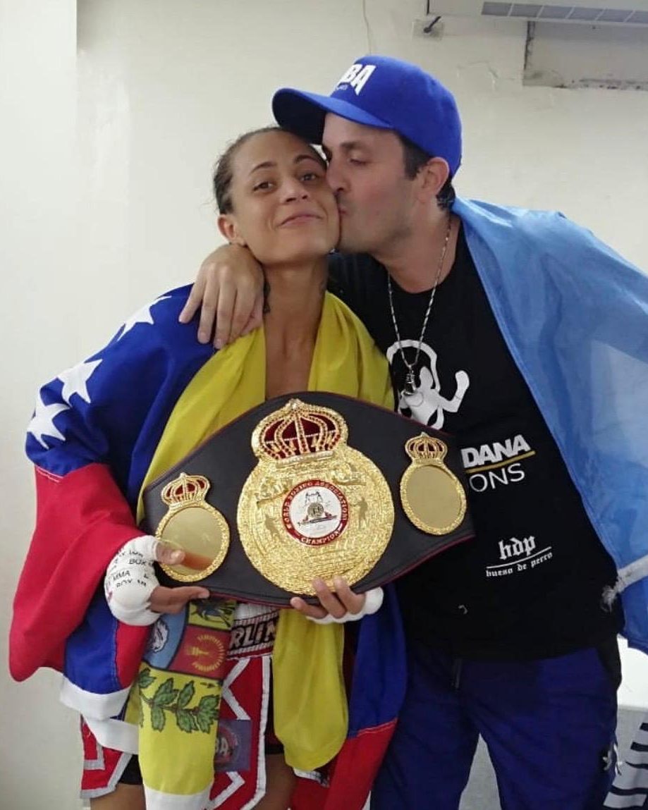 Mayerlin Rivas, envuelta en la bandera de Venezuela, sostiene el cinturón de la Asociación Mundial de Boxeo mientras Calabrese, con la bandera argentina sobre los hombros, le da un beso en la mejilla